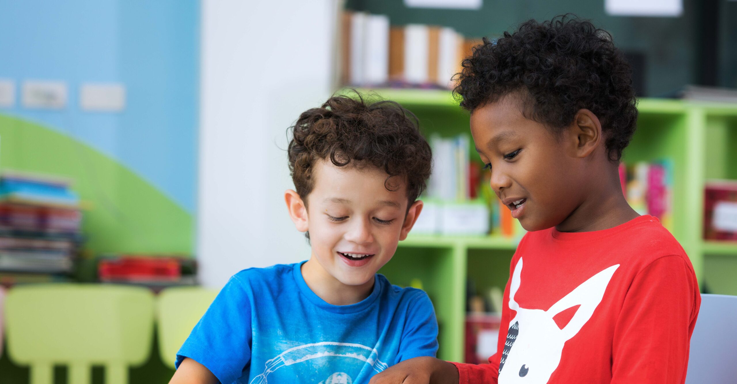 Two boys of different ethnicities reading together at school.