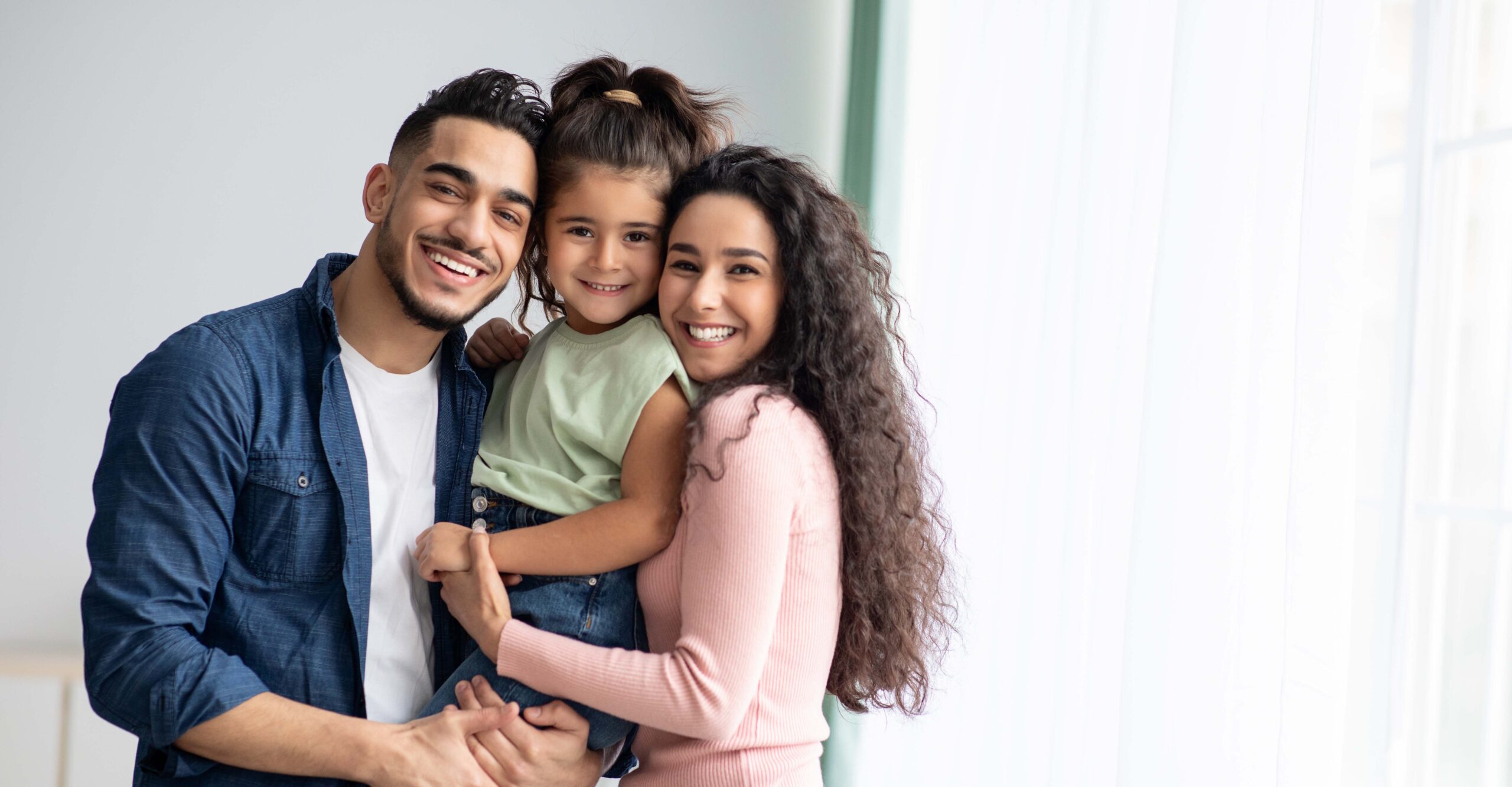 A happy mother and father holding their young daughter, and everyone is smiling.